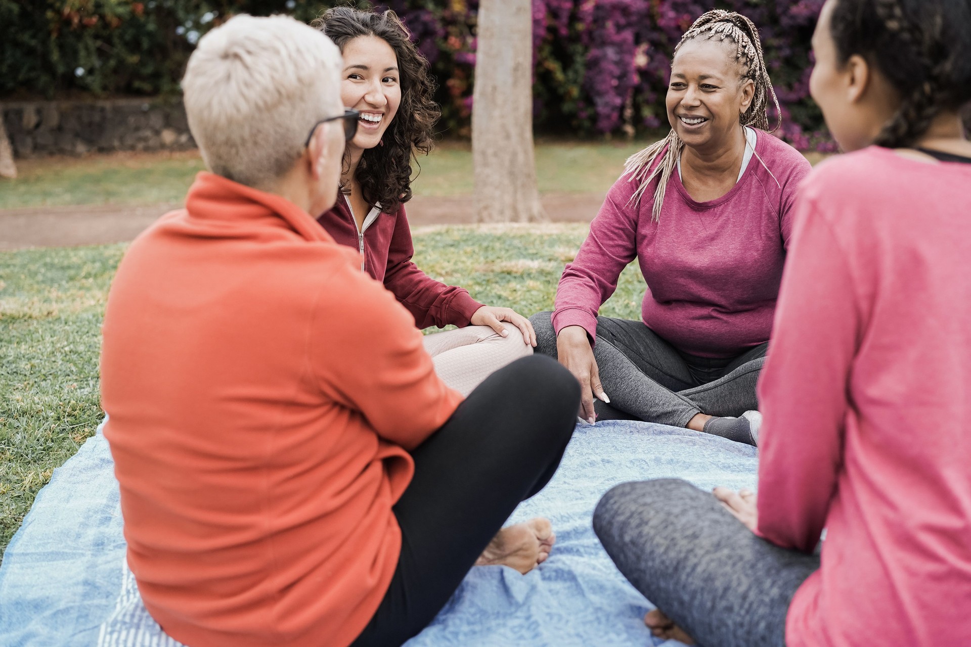 Happy multi generational women having fun together sitting outdoors at city park - Focus on african senior face